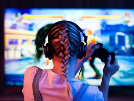 A gamer or a streamer girl at home in a dark room with a gamepad playing with friends on the networks in video games. A young man sits in front of a monitor or TV.